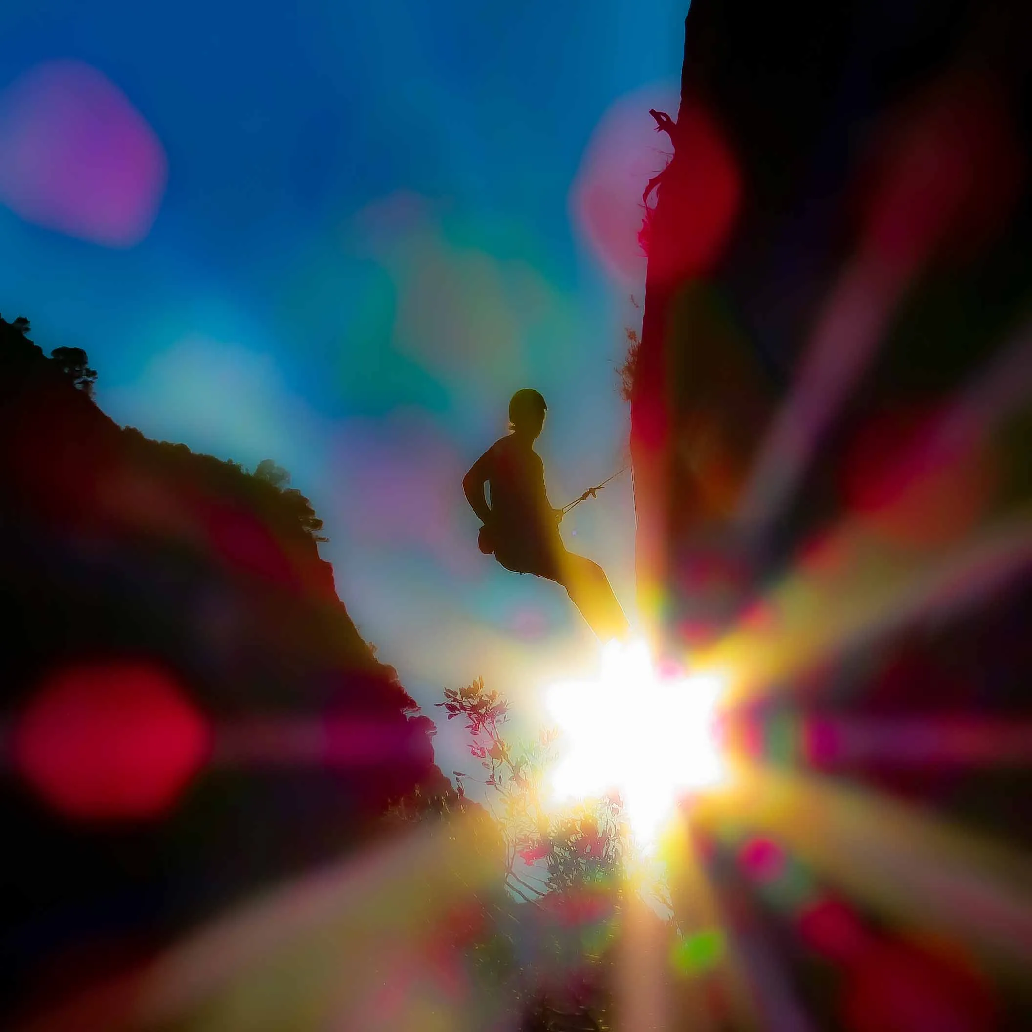 A climber silhouetted above a bright sun flare